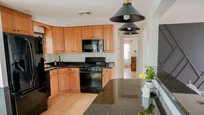 Una cocina moderna con armarios de madera, un refrigerador negro, una estufa y una encimera de granito.