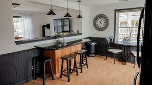 Una cocina moderna con una isla central, taburetes de bar, iluminación colgante, un reloj grande y una ventana con vistas.