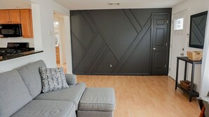 Una sala de estar moderna con un sofá gris, una pared de acento oscura y piso de madera.