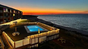 A rooftop pool area with a view of the ocean at sunset, surrounded by a fence and lounge chairs. - Palm Beach Oasis - Soundfront - Quiet (Pensacola Beach)