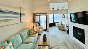 A spacious living room with a sofa, coffee table, and a TV. There is a balcony with a view of the sea. - Palm Beach Oasis - Soundfront - Quiet (Pensacola Beach)