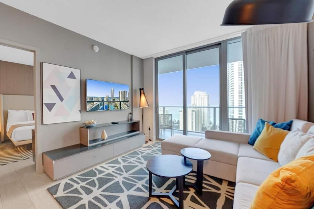 A modern hotel room with a bed, a sofa, a TV, and a city view.