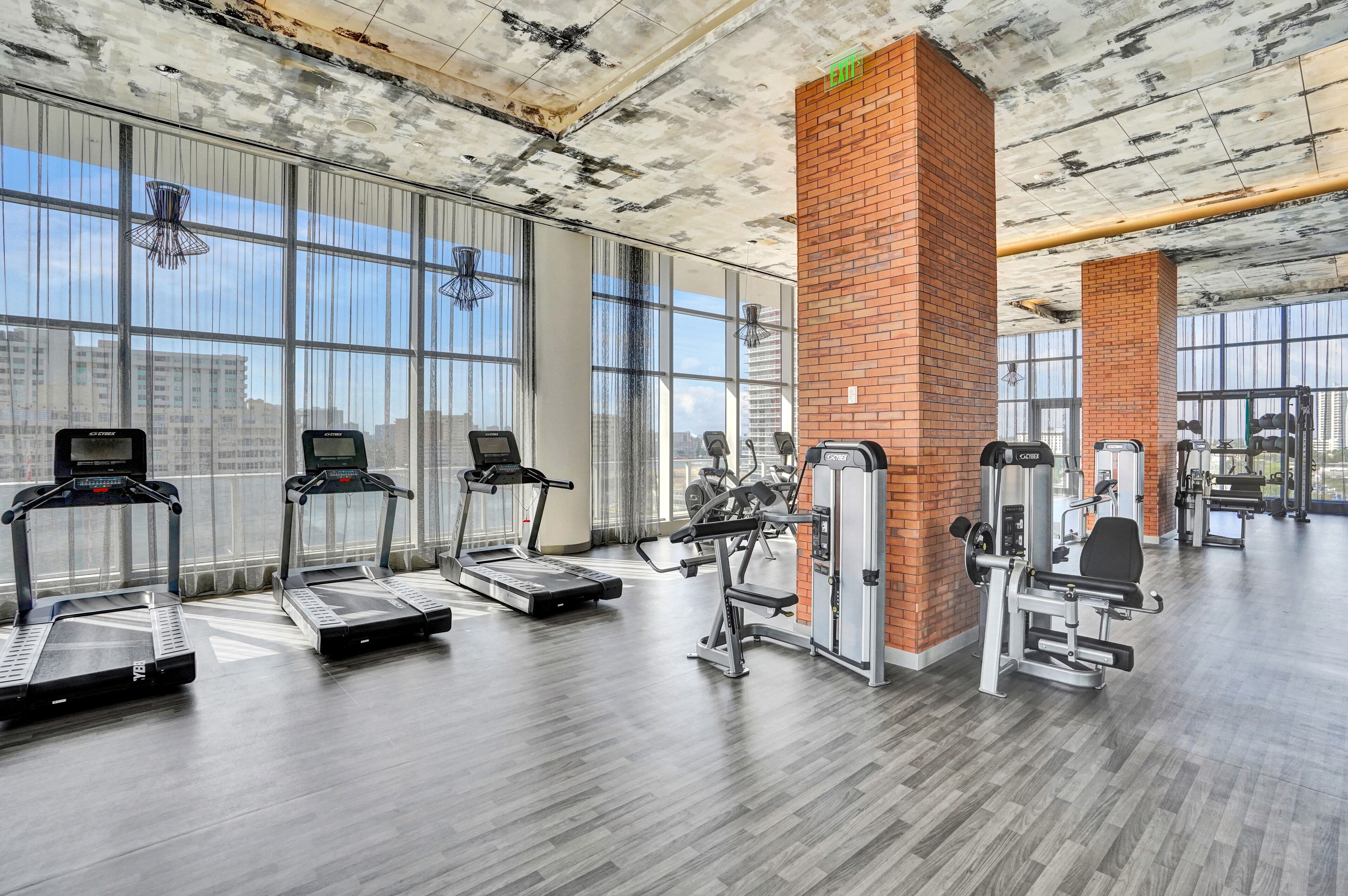 A gym with treadmills, weight machines, and large windows offering city views.