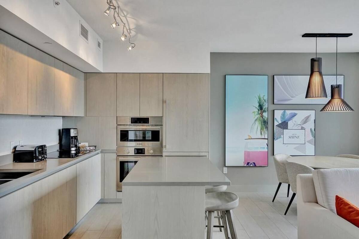 A modern kitchen with stainless steel appliances, a central island, and a dining area with a white table and bar stools.
