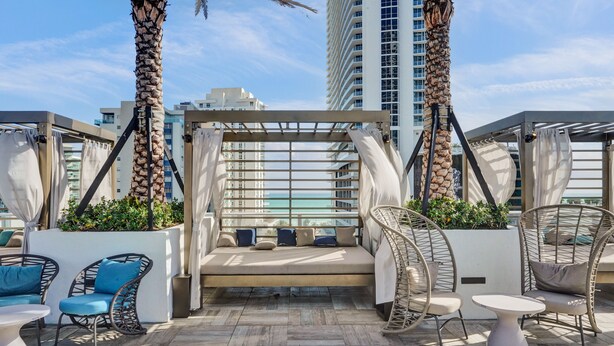 A rooftop lounge with a cushioned seating area, wicker chairs, and a view of the city skyline. - Amazing Apartments at H Beach House (Hollywood)