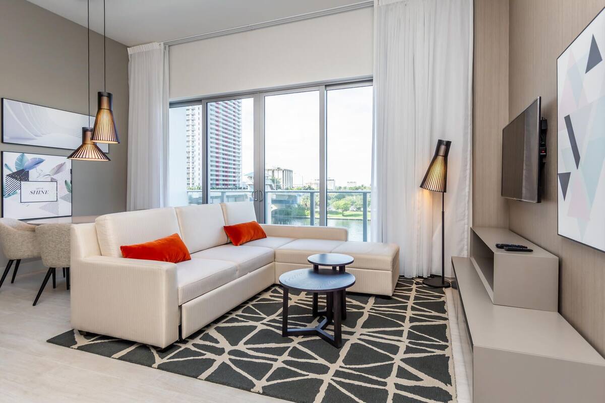 A modern living room with a sectional sofa, a small round table, and a TV mounted on the wall.