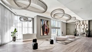A spacious lobby with a modern design, featuring a large abstract painting, a reception desk, and a seating area with ottomans. - Amazing Apartments at H Beach House (Hollywood)
