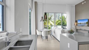 A modern kitchen with a dining area, large windows with curtains, and a view of palm trees and buildings. - Amazing Apartments at H Beach House (Hollywood)
