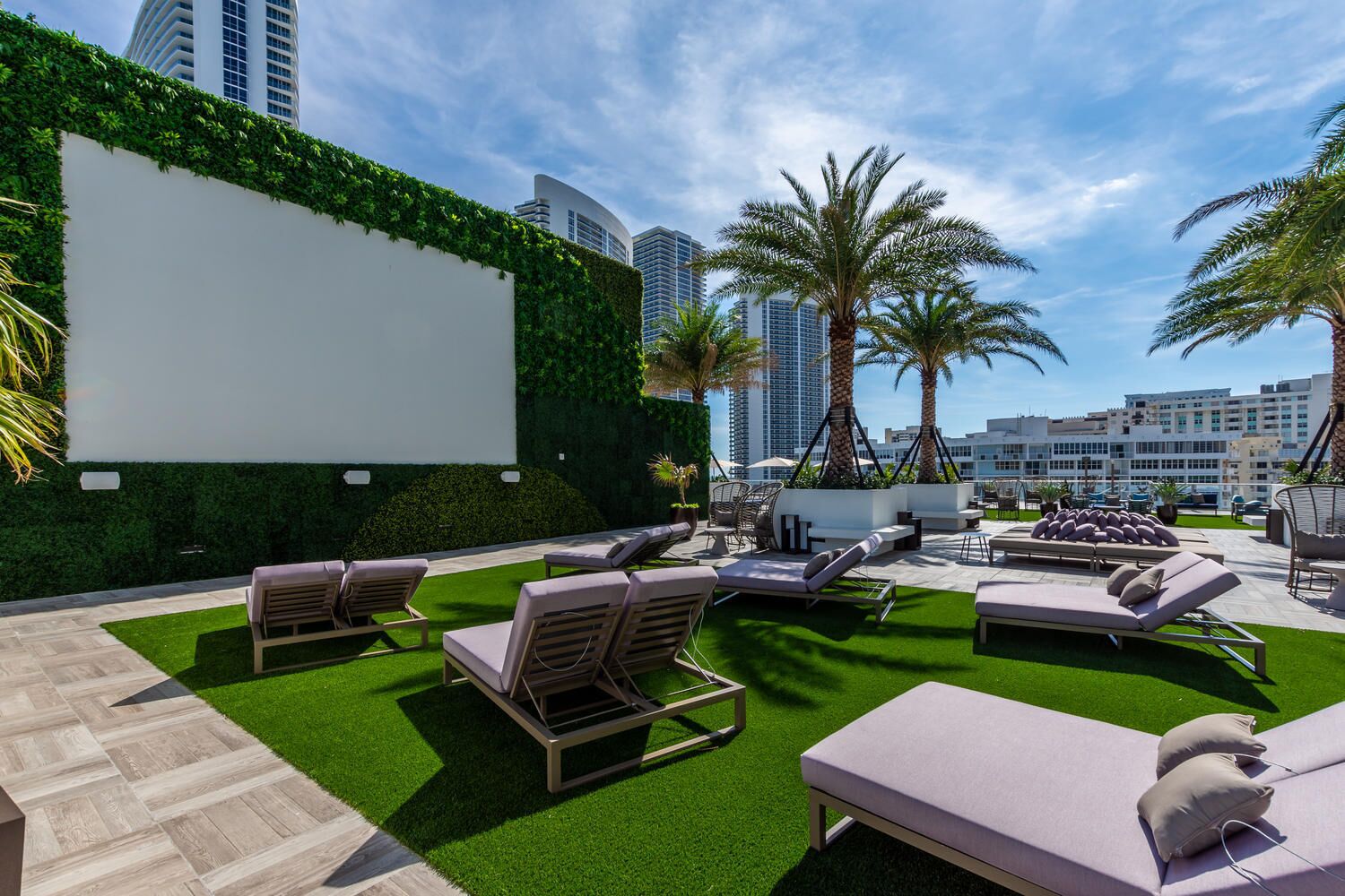 A rooftop lounge with outdoor seating, a large blank screen, and palm trees.