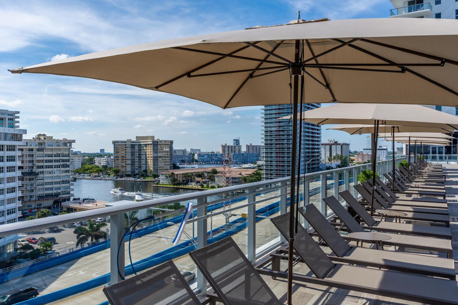 Terraza en la azotea con sillones solárium y sombrillas, con vistas a un puerto deportivo y al paisaje urbano.
