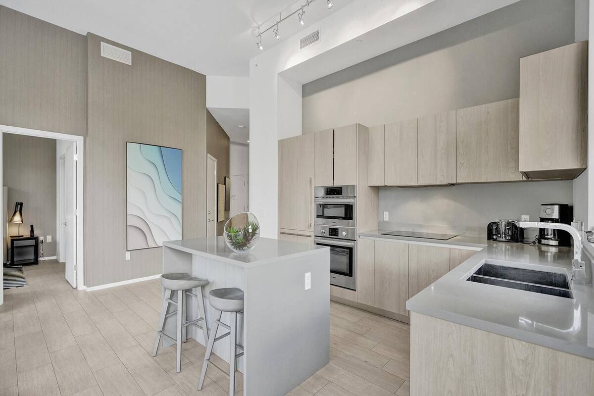 A modern kitchen with light wood cabinets, stainless steel appliances, and a central island with stools.
