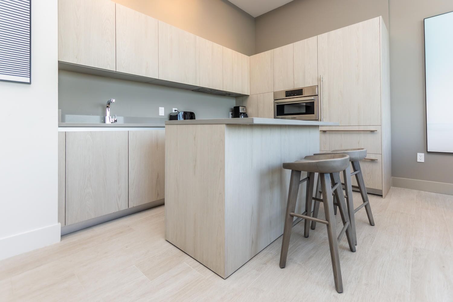 Une cuisine moderne avec des meubles de couleur bois clair, un îlot central doté de tabourets et des appareils électroménagers intégrés.