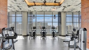 A gym with exercise equipment, large windows, and a view of the city. - Amazing Apartments at H Beach House (Hollywood)