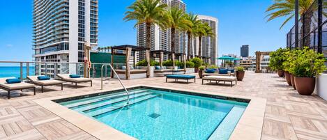 A rooftop pool area with lounge chairs and a view of tall buildings.
