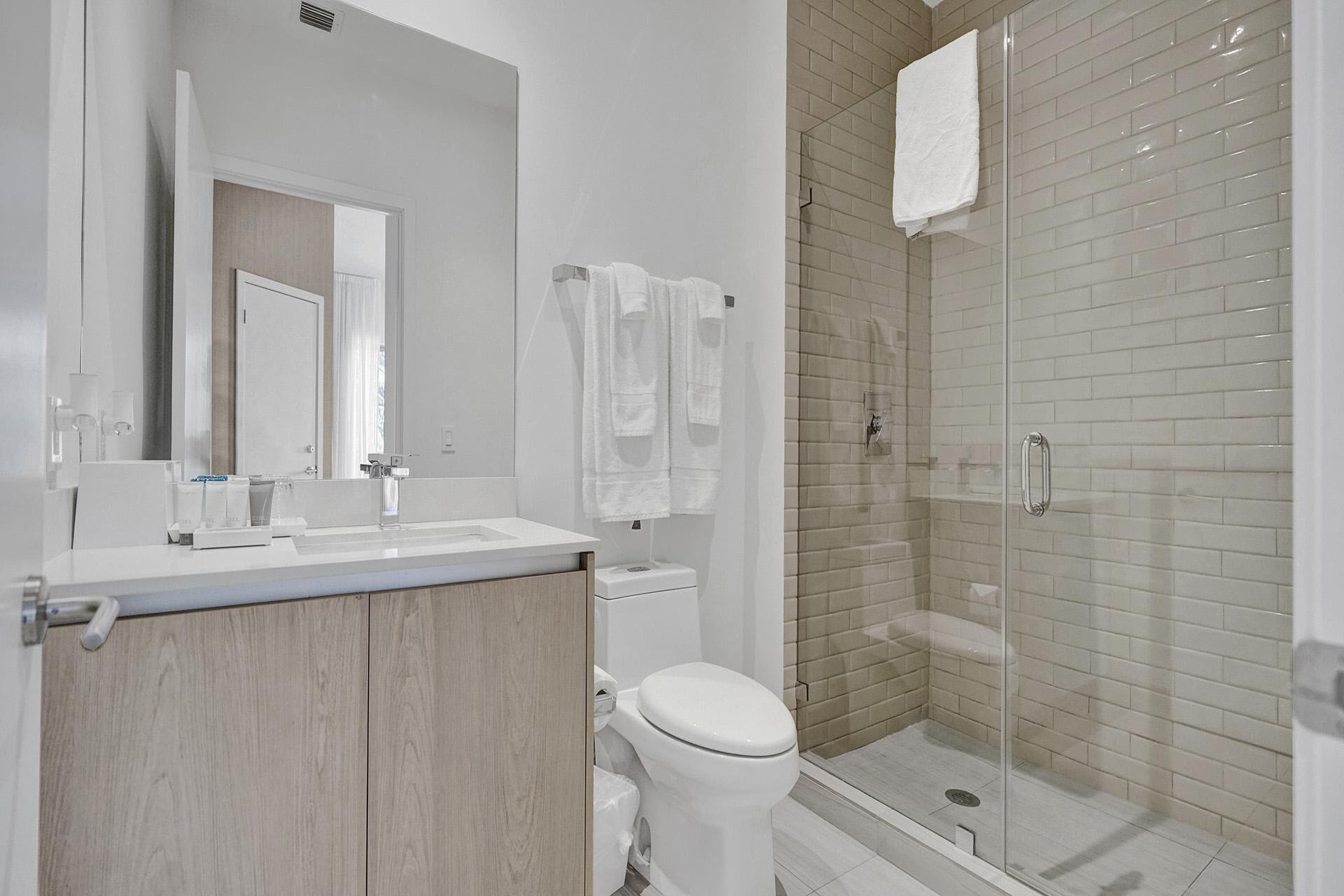 Ein modernes Badezimmer mit Waschbecken, Spiegel und Toilette. Es verfügt über eine Dusche mit Glastrennwand und befliester Wand.