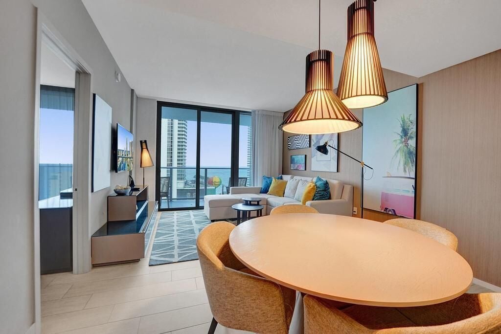 A modern living room with a round wooden table, two sofas, and a large window offering a city view.