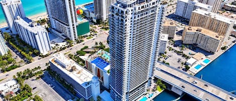 A high-rise hotel with multiple balconies, a swimming pool, and a view of the ocean.