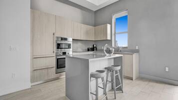 A modern kitchen with a central island, stainless steel appliances, light wood cabinetry, and a large window providing natural light.