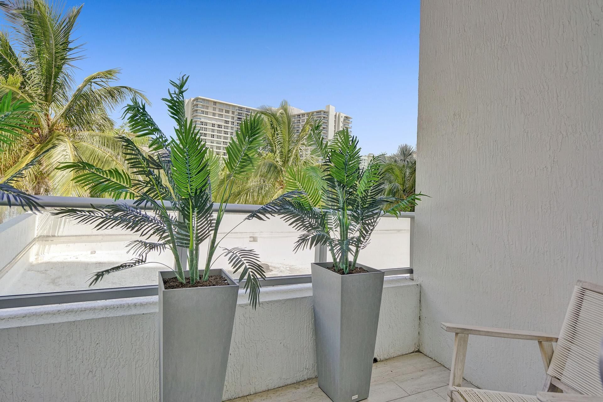 A balcony with two potted plants, a white chair, and a view of tall buildings.