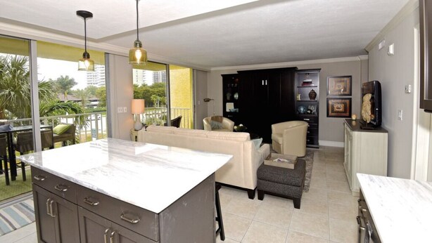 A modern kitchen with a marble countertop, a dining area with a table and chairs, a sofa, and a black cabinet with decorative items. - Renovated  Condo with Luxury Amenities in Perfect Beach Location (Marco Island)