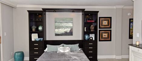 A bedroom with a bed, built-in shelving, and artwork on the walls.