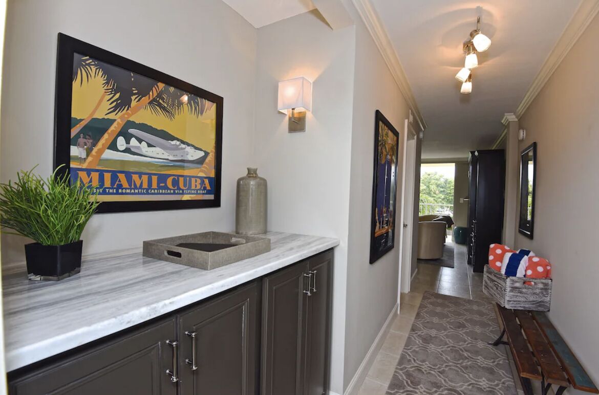 A hallway with a framed poster, a potted plant, a marble countertop, and a bench.