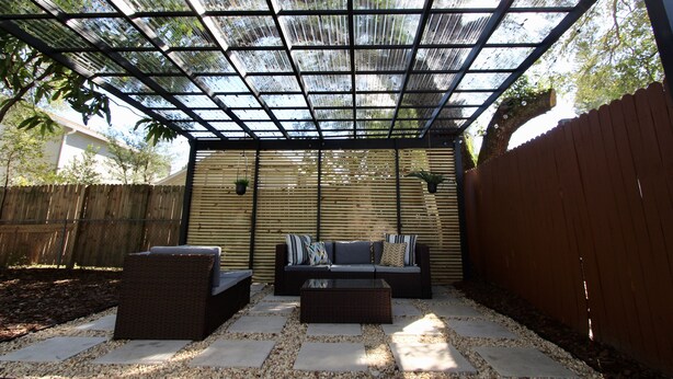 Ein überdachter Patio-Bereich mit einer Sitzecke, inklusive einer Couch und zwei Sesseln sowie einem Couchtisch.