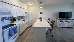 Uma cozinha moderna com armários brancos, uma ilha central e uma área de refeições com cadeiras.