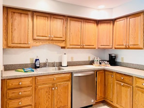 A kitchen with wooden cabinets, a stainless steel sink, a dishwasher, and a coffee maker.