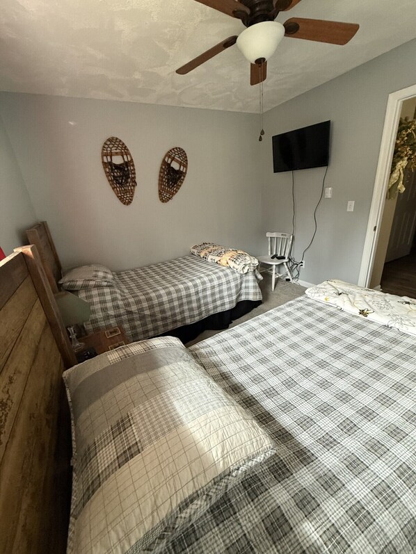 A bedroom with two beds, a ceiling fan, a TV mounted on the wall, and a chair. - cabin on a stream (Sugar Grove)