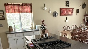 Een keuken met een gasfornuis, witte kasten, een rood-wit geruit kleed en een eethoek met een houten tafel en stoelen.