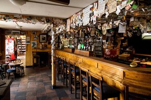 Un bar avec un comptoir en bois, des tabourets et un mur recouvert de divers papiers et notes.