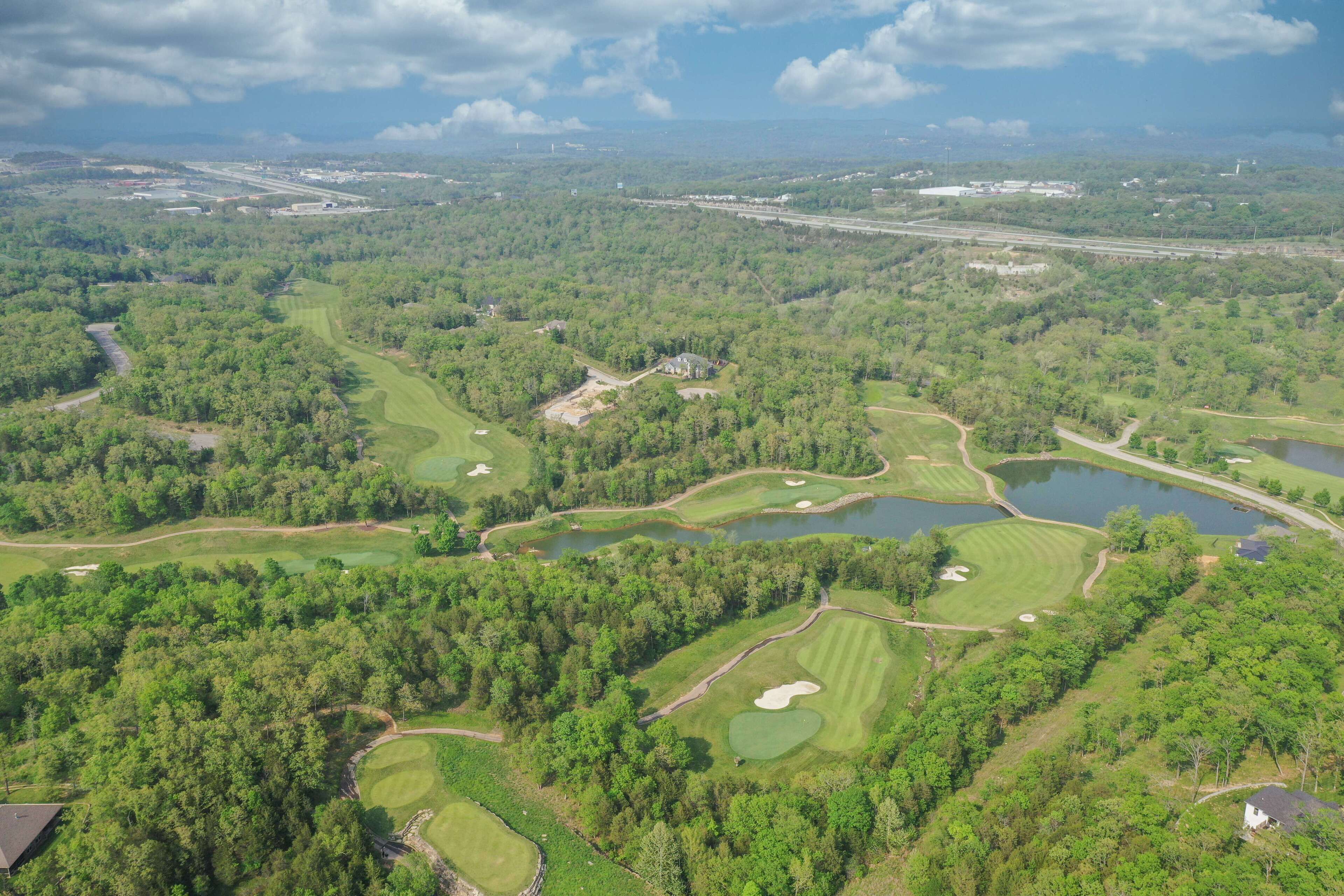 Eine Vogelperspektive auf einen Golfplatz mit mehreren Grüns, Wasserhindernissen und einem Clubhaus.