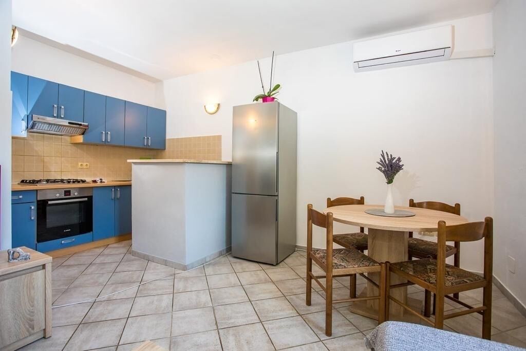Una cocina compacta con gabinetes azules, un refrigerador de acero inoxidable, una estufa a gas y una mesa de comedor con sillas.