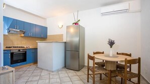 A compact kitchen with blue cabinets, a stainless steel refrigerator, a gas stove, and a dining table with chairs. - Natura-Gata,Omiš-small stone apartman with swimming pool (Gata)