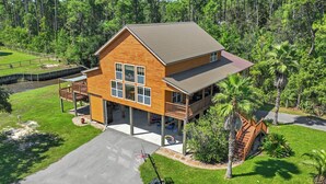 A two-story wooden house with a balcony, surrounded by lush greenery and a small pond. - Pool, Boat Ramp, Games, Pass Christian Waterfront Sleeps 18 Guests 6 Bedrooms (Pass Christian)