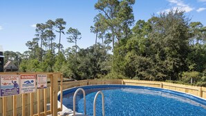 An outdoor swimming pool with wooden deck and safety signs, surrounded by trees. - Pool, Boat Ramp, Games, Pass Christian Waterfront Sleeps 18 Guests 6 Bedrooms (Pass Christian)