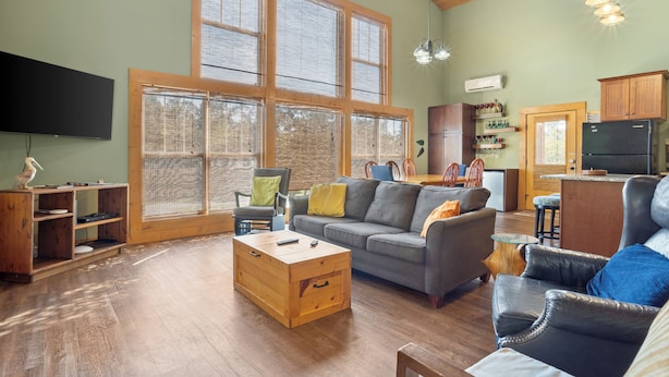 A spacious living room with a large window, a wooden coffee table, a grey sofa, and a black leather chair. - Pool, Boat Ramp, Games, Pass Christian Waterfront Sleeps 18 Guests 6 Bedrooms (Pass Christian)