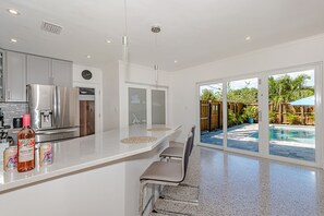 A modern kitchen with stainless steel appliances, a white countertop, and a view of a backyard with a pool.