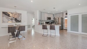 Eine moderne Küche mit einer zentralen Kochinsel, Barhocker, Edelstahlgeräten und einem großen abstrakten Gemälde an der Wand.