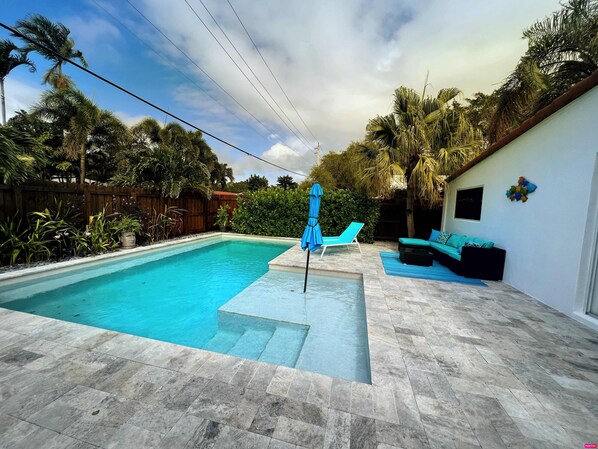 A swimming pool with a tiled deck, a lounge chair, and a sofa.