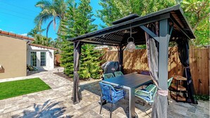 Eine Terrasse im Freien mit einer Pergola, einem Grill und einem Esstisch mit Stühlen.