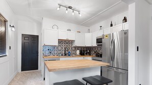 Eine moderne Küche mit weißen Schränken, einem Edelstahlkühlschrank, einer Holz Arbeitsplatte und schwarzen Barhocker.