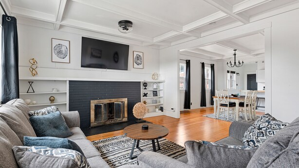 Ein modernes Wohnzimmer mit Kamin, grauen Sofas und einem Essbereich mit einer Chandelüster.