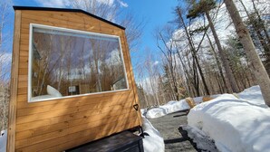 Una cabaña de madera con un ventanal grande, rodeada de nieve y árboles.