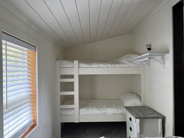 A bunk bed room with a window, a small desk, and a wall-mounted shelf.