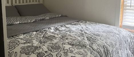A bedroom with a bed, a window with blinds, and a white ceiling.