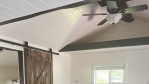 Une pièce comprenant un canapé d’angle, une porte coulissante de style rustique et un ventilateur de plafond.