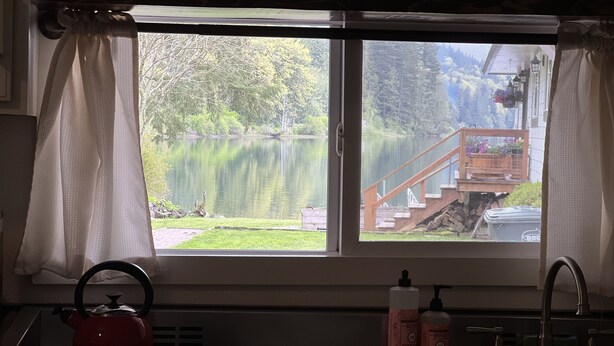 Une cuisine avec une fenêtre donnant sur un lac et une terrasse en bois.