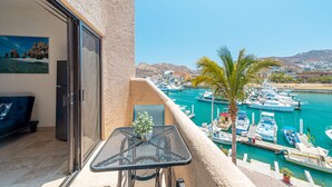 A balcony with a table and chairs, overlooking a marina with boats and a mountain in the background. - Marina View Open Studio Suite on Marina 645SF walk everywhere! NEW Rooftop Pool (Cabo San Lucas)